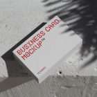 View from above, outdoor business card mockup with red and white colors, geometric typography design laying on the white color concrete.