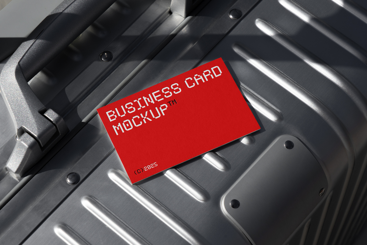 View from above, single outdoor business card mockup with red and white colors, geometric typography design, laying on an aluminum Rimowa brand suitcase.