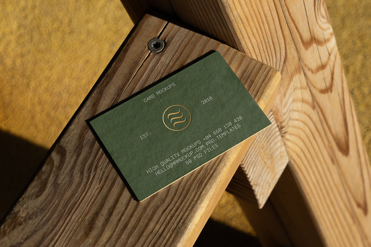 View from above, single outdoor business card mockup with green and gold colors, serif typography design, laying on the wooden balcony railing.