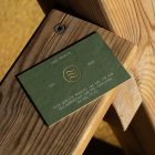 View from above, single outdoor business card mockup with green and gold colors, serif typography design, laying on the wooden balcony railing.