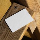 View from above, a single blank outdoor business card mockup laying on the wooden balcony railing.