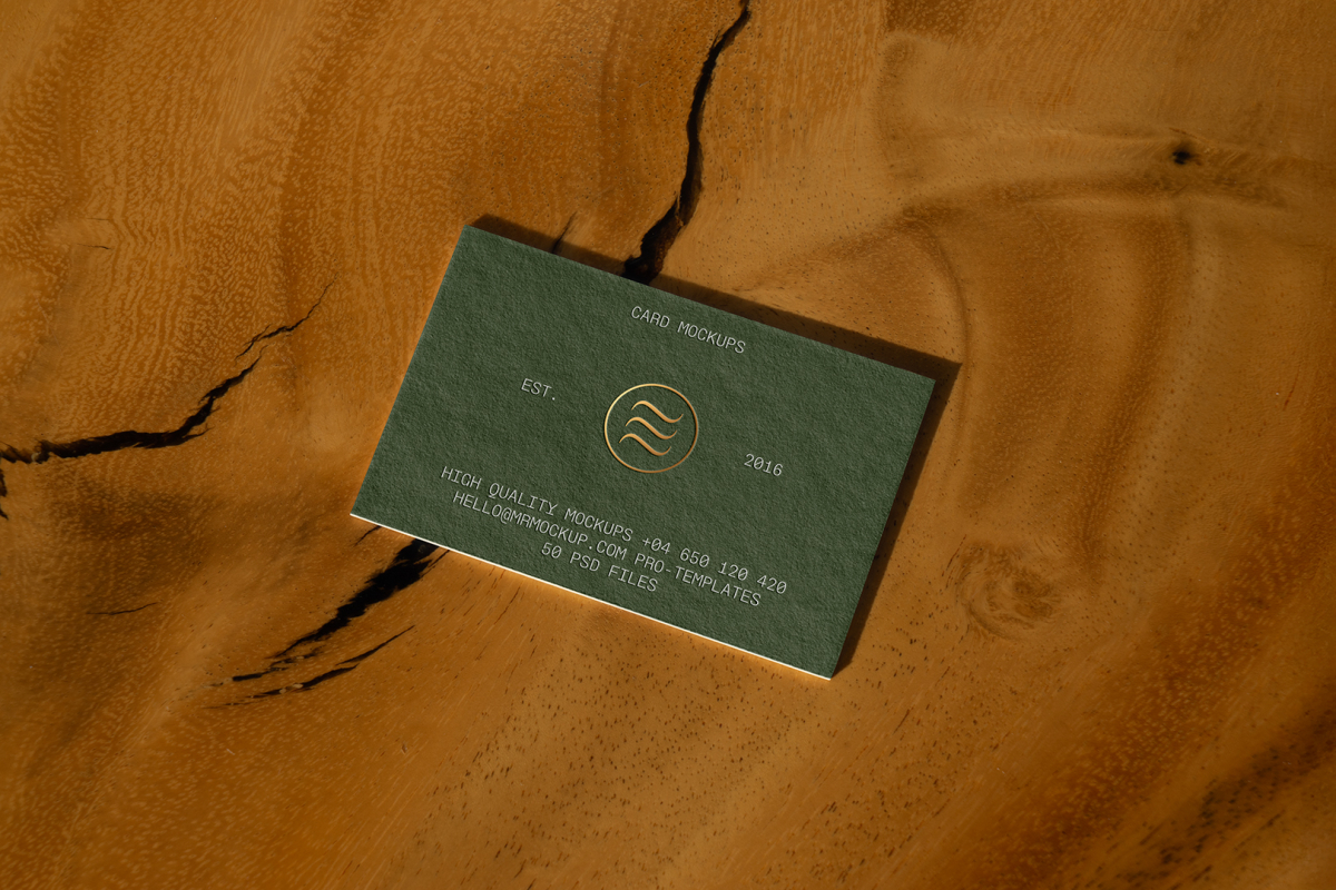 View from above, single outdoor business card mockup with green and gold colors, serif typography design, laying on the wooden background.