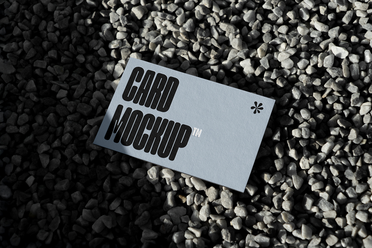 View from above, single outdoor business card mockup with blue and black colors and strong design, laying lies on the little pebbles.