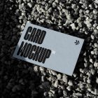 View from above, single outdoor business card mockup with blue and black colors and strong design, laying lies on the little pebbles.