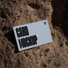 View from above, single outdoor business card mockup with blue and black colors, strong typography design, laying on massive stone.