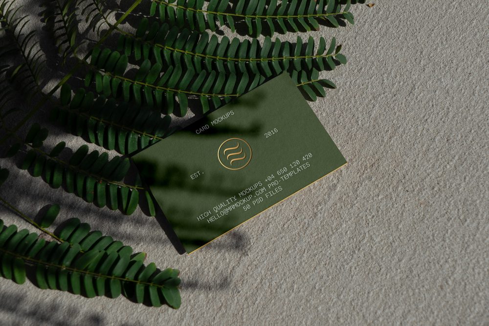 View from above, single outdoor business card mockup with green and gold colors, serif typography design, laying on the sand background.