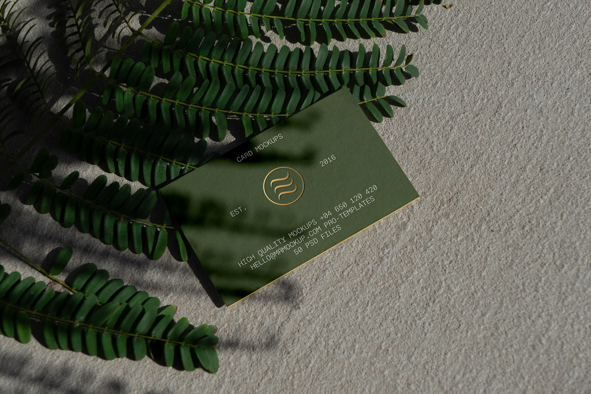 View from above, single outdoor business card mockup with green and gold colors, serif typography design, laying on the sand background.
