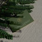 View from above, single outdoor business card mockup with green and gold colors, serif typography design, laying on the sand background.