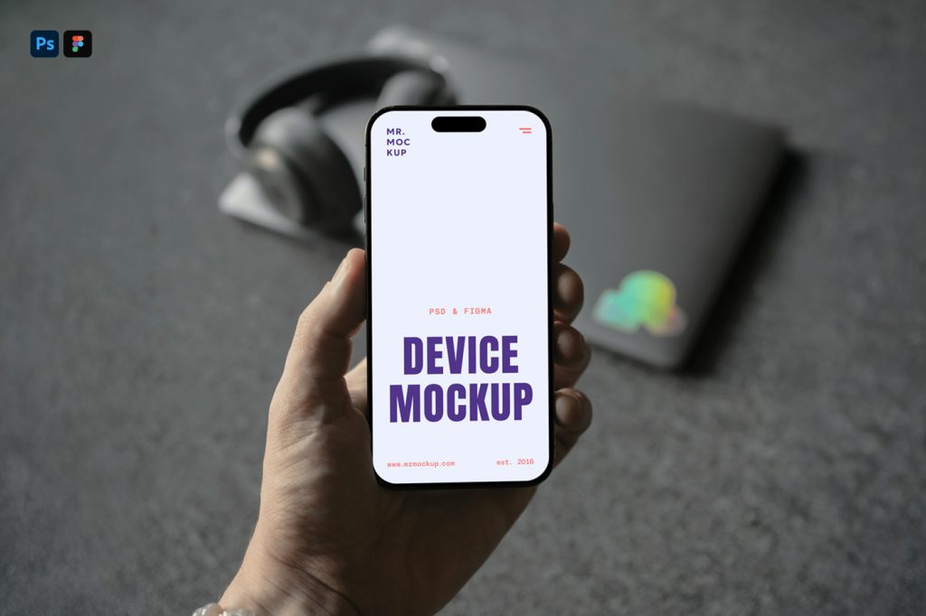 Front view, Hand Holding iPhone Mockup and visible blurred headphones and laptop laying on the dark gray carpet behind.