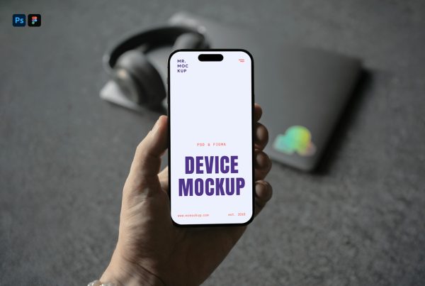 Front view, Hand Holding iPhone Mockup and visible blurred headphones and laptop laying on the dark gray carpet behind.