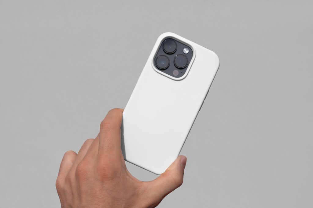 Front view, Hand Holding white iPhone Case Mockup with visible gray wall behind.