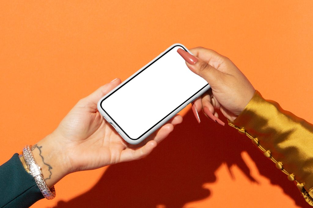 Front view, passed from hand to hand iPhone 16 Pro Mockup with white screen and white case with visible orange color wall behind.