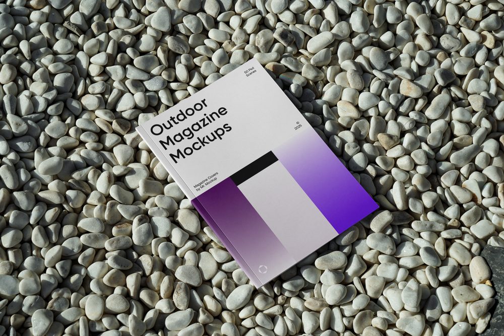 View from above, a single outdoor magazine mockup with three gradient shades and strong typography design lying on the pebbles.