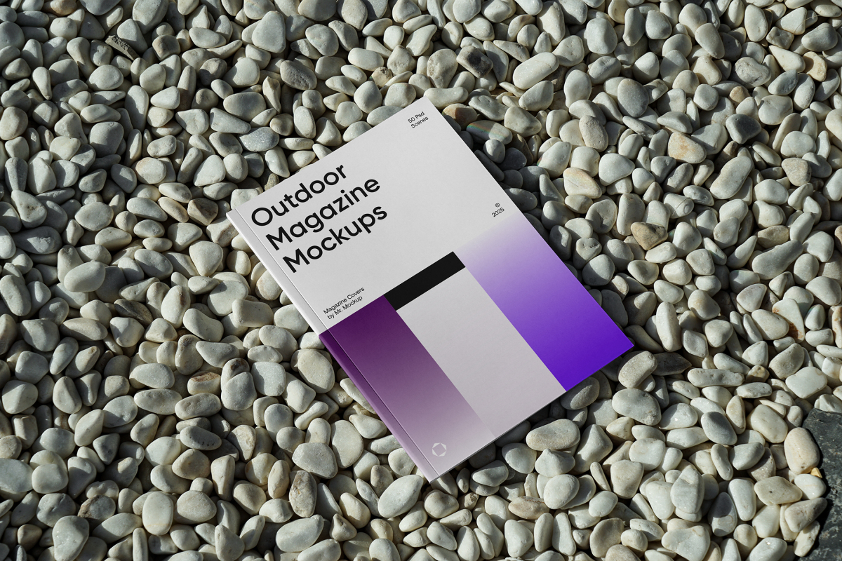 View from above, a single outdoor magazine mockup with three gradient shades and strong typography design lying on the pebbles.