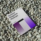 View from above, a single outdoor magazine mockup with three gradient shades and strong typography design lying on the pebbles.