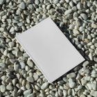 View from above, a single white outdoor magazine mockup lying on the pebbles.