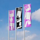 Front view, Three Vertical Flag Mockups with white, black, and pink designs against the sky background. Scene from our Museum Mockups product.