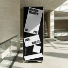 Front view, Vertical Stand Mockup with white and black design standing inside the modern architecture building. Scene from our Museum Mockups product.