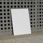 Front view, a white outdoor magazine mockup resists on a concrete wall with a square pattern.