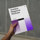 Front view of an outdoor magazine mockup holding by a man's hand with three gradient shades and strong typography design on a concrete wall with a square pattern in the background.