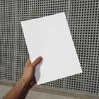 Front view of a white outdoor magazine mockup holding by a man's hand on a concrete wall with a square pattern in the background.