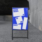 Front view, Poster Mockup with black metal frame and white and blue design. Standing on the patio. Scene from our Museum Mockups product.
