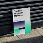 Front View, Outdoor Magazine Mockup with three gradient shades and strong typography design resists on metal fence in black color.