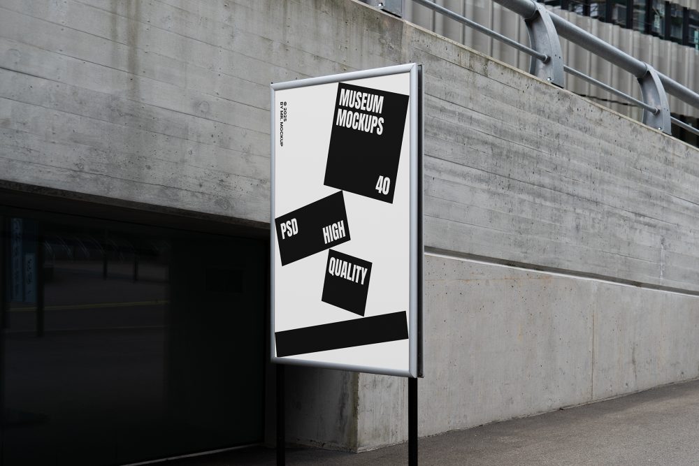 Front view, Poster Mockup with white and black design holding on a black metal pole. Standing against the background of a gray concrete wall. Scene from our Museum Mockups product.