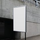 Front view, White Poster Mockup holding on a black metal pole. Standing against the background of a gray concrete wall. Scene from our Museum Mockups product.