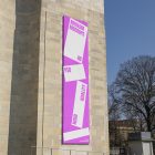 Front view, Vertical Billboard Mockup with white and pink design attached to the old building against the sky. Scene from our Museum Mockups product.