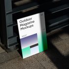 Front View, Outdoor Magazine Mockup with three gradient shades and strong typography design resists on metal fence in black color.