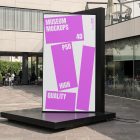 Front view, Vertical Billboard Mockup with white and pink design attached to the black metal landing. In the background you can see people sitting at tables. Scene from our Museum Mockups product.