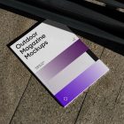 View from above of an Outdoor Magazine Mockup with three gradient shades and strong typography design lying on marble under a metal fence in black color.