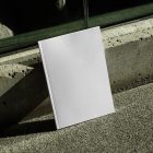 Front view, a white outdoor magazine mockup resists on a concrete curb.