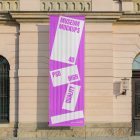 Front view, Hanging Vertical Banner Mockup with white and pink design attached to the silver pole in front of the old building elevation. Scene from our Museum Mockups product.