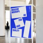 Front view, Poster Mockup with white and blue design and white metal frame standing inside the building. Scene from our Museum Mockups product.