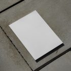 View from above of a white outdoor magazine mockup lying on concrete slabs.