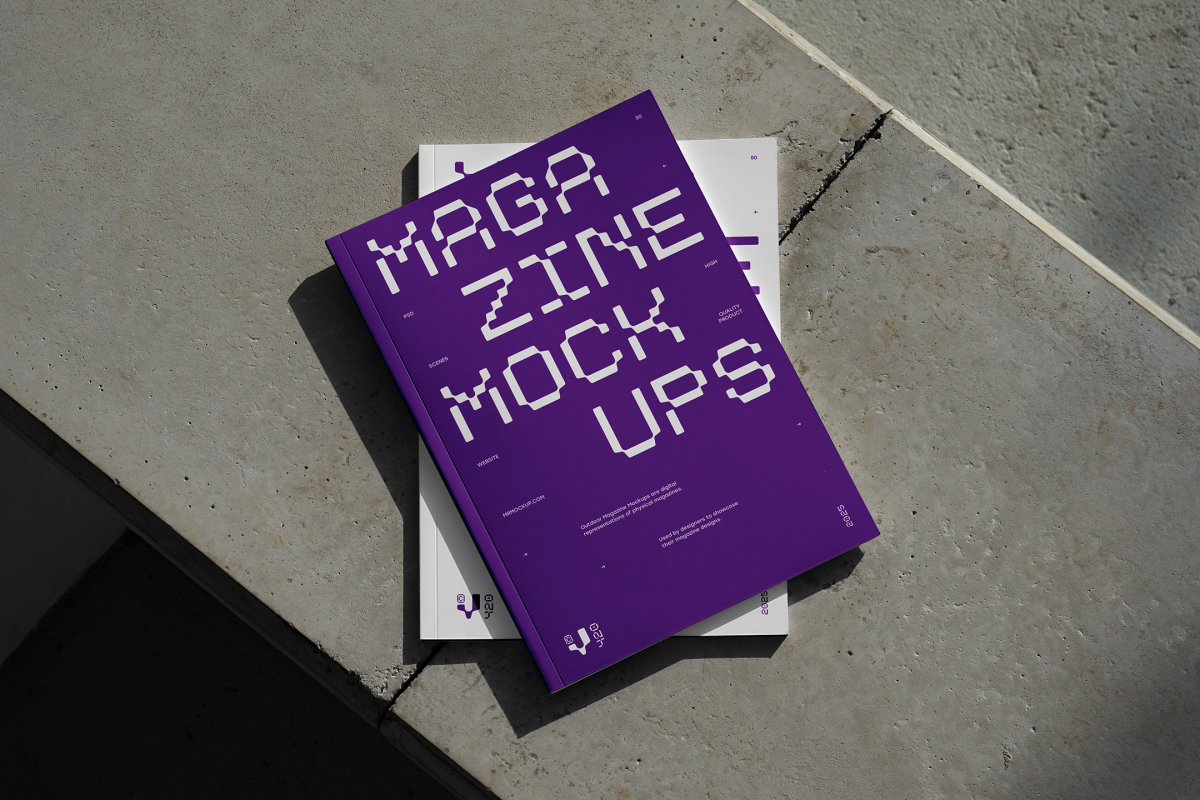 View from above of an Two Outdoor Magazine Mockup with strong purple typography design lying on concrete slabs.