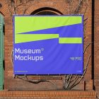 Front view, Rectangle Banner Mockup with white, purple, and neon green geometric design attached to the classic brick colored wall on an old building elevation. Scene from our Museum Mockups product.