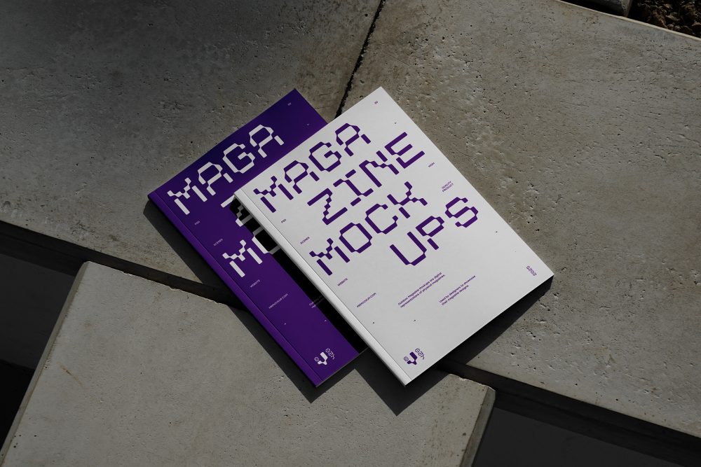 View from above of an Two Outdoor Magazine Mockup with strong purple typography design lying on concrete slabs.