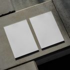 View from above of two white outdoor magazine mockups lying on concrete slabs.