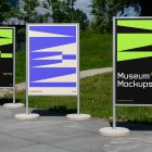 Front view, Three Poster Mockups with white, black, beige, and purple geometric designs standing on the side wall in front of the city park. Scene from our Museum Mockups product.