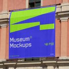 Front view, Rectangle Banner Mockup with white, purple, and neon green geometric design hanging on the old building elevation. Scene from our Museum Mockups product.