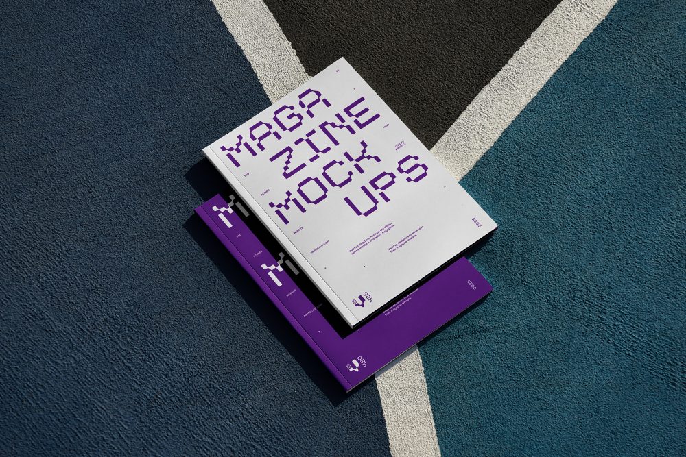 View from above of two outdoor magazine mockups with strong purple typography designs lying on a basketball court.