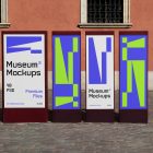 Front view, Four Vertical Poster Mockups with white, black, purple, and neon green geometric designs standing in front of the old building. Scene from our Museum Mockups product.
