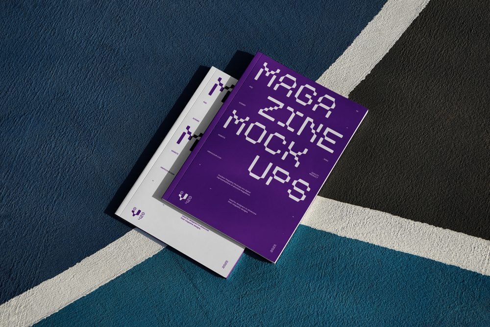 View from above of two outdoor magazine mockups with strong purple typography designs lying on a basketball court.