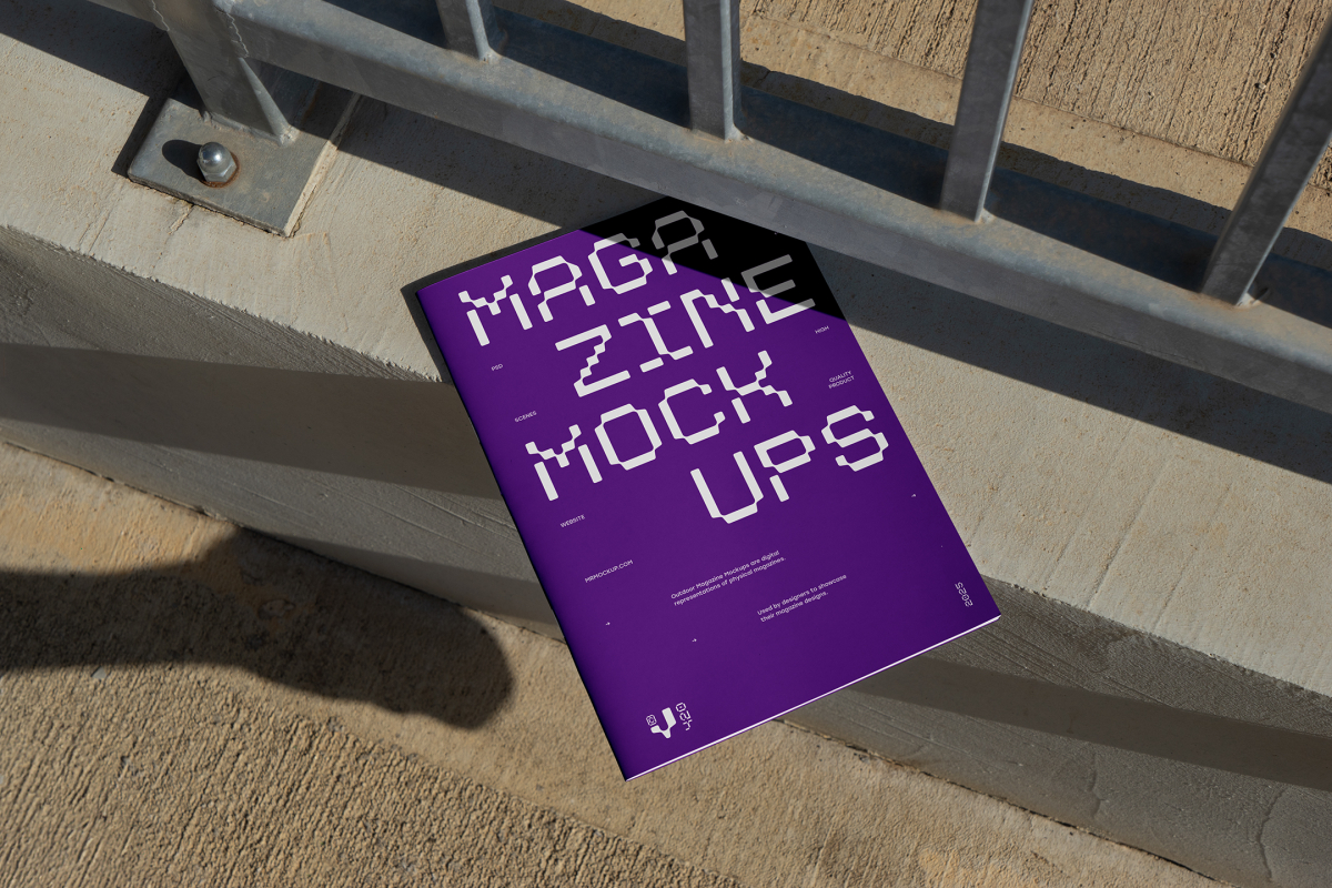 View from above of outdoor magazine mockups with strong purple typography design lying on concrete under a metal fence in silver color.