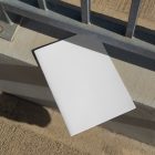 View from above of a white outdoor magazine mockup lying on concrete under a metal fence in silver color.