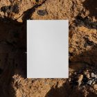 Front view, a white outdoor magazine mockup standing on the boulders.