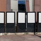 Front view, Five White Poster Mockups standing in front of the modern architecture building. Scene from our Museum Mockups product.
